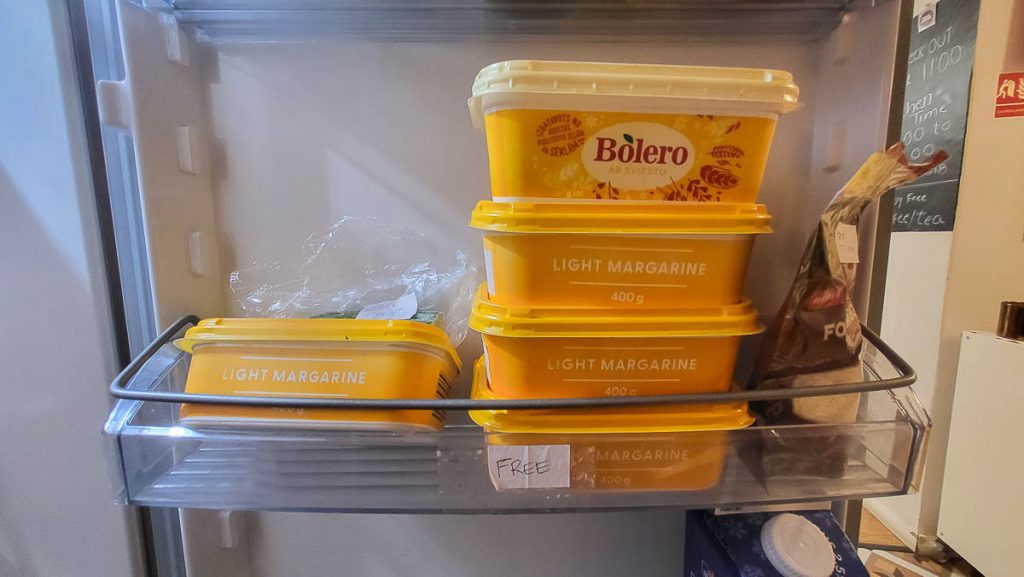 A fridge door compartment filled with yellow margarine containers, labeled 'Light Margarine' and 'Bolero ar sviestu.' A small sign reading 'FREE' is attached to the shelf, indicating the margarine is available for hostel guests.