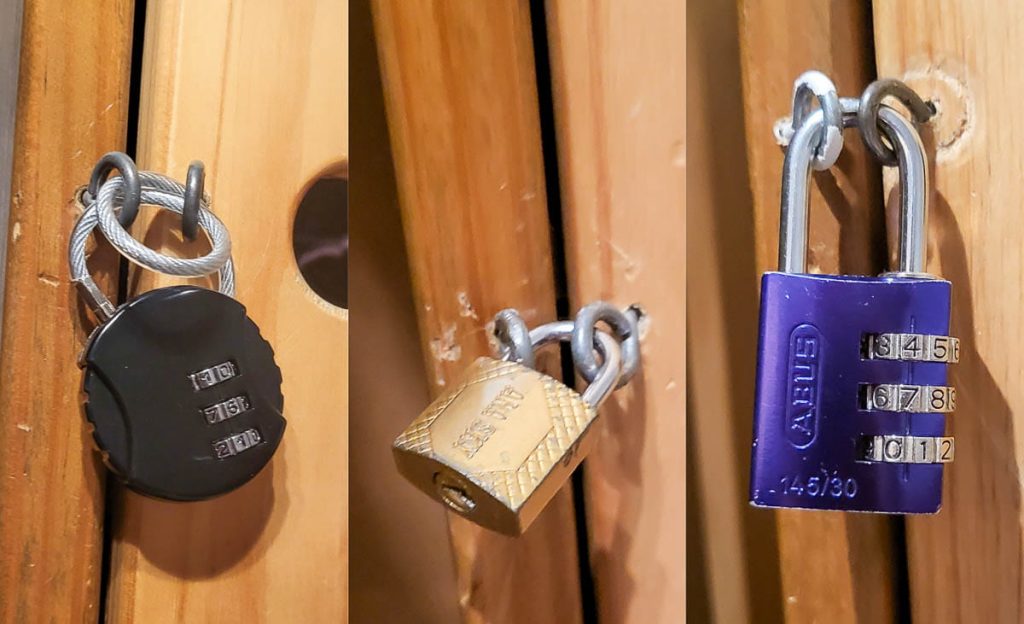 A close-up of three different padlocks securing wooden lockers: a black combination lock, a gold key lock, and a purple combination lock. The lockers appear slightly worn from use.